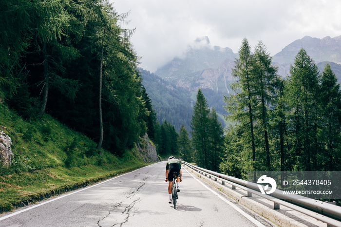 Professional road cyclist on fast and light carbon bicycle descends mountain road in Alps Dolomites. Fit and athletic man on recreational ride trip or training camp, enjoy time outdoors on bike