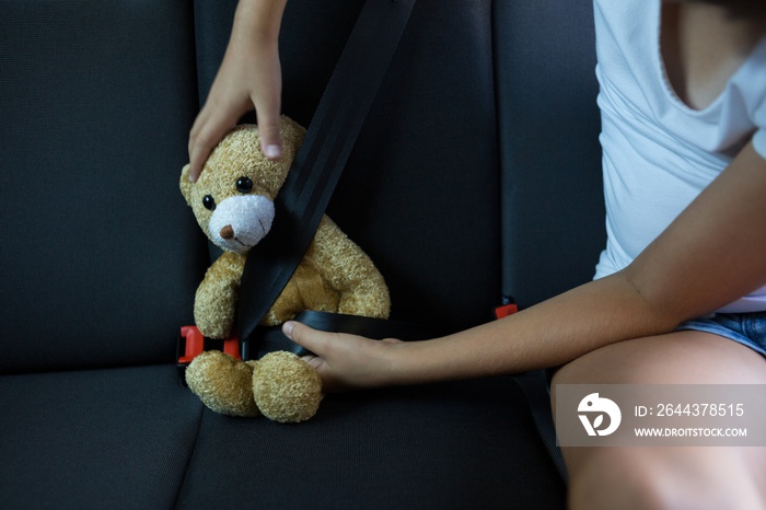 Teenage girl sitting with teddy bear in the back seat of car