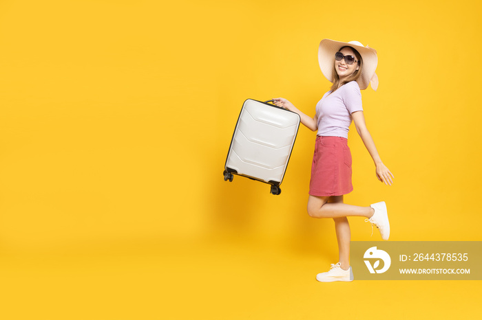 Happy Asian woman traveler standing and holding suitcase isolated on yellow background, Tourist girl having cheerful holiday trip concept, Full body composition