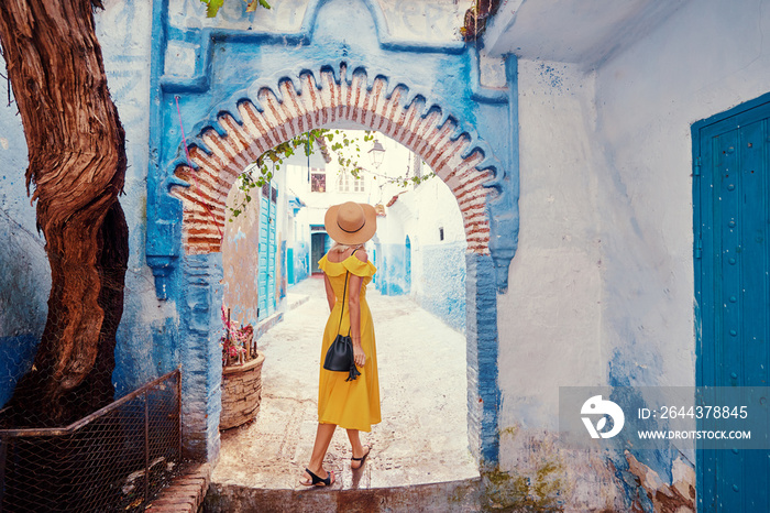 Colorful traveling by Morocco. Young woman in yellow dress walking in  medina of  blue city Chefchaouen.