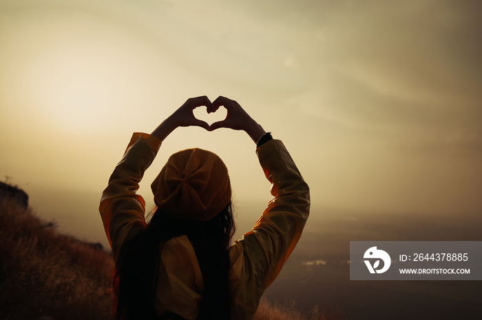 A young girl making heart symbol with her hands at sunset