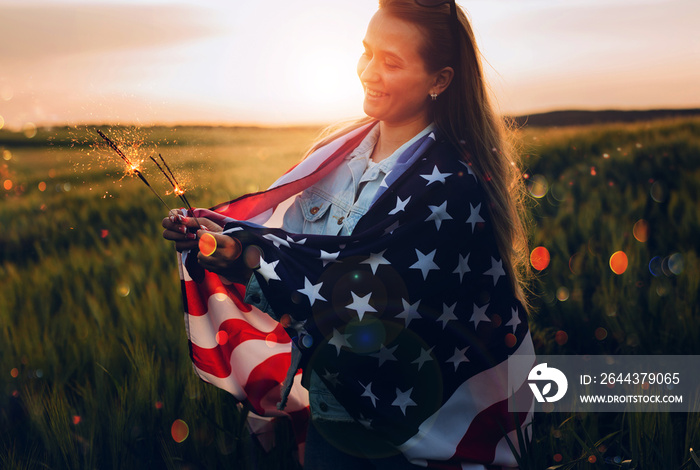 America celebrate 4th of July. Independence Day. Young woman holding bengal fire with American flag at sunset.