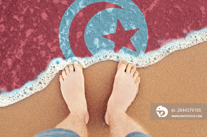 Two feet on beach with flag Tunisia. Top View on sea wave.