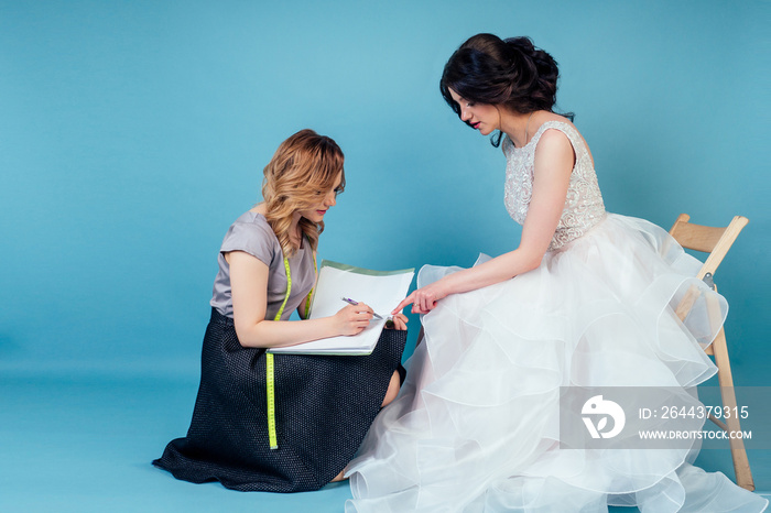 seamstress wedding consultant and bride discuss the details of party wedding dress in the studio on a blue background . tailor dressmaker and customer prom in the dressing room next to the mirror