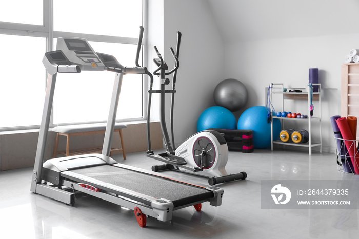 Interior of gym with modern treadmill and sport equipment near window