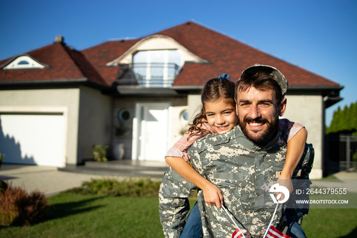 Portrait of father soldier in uniform on military leave holding his lovely daughter in front of their house.