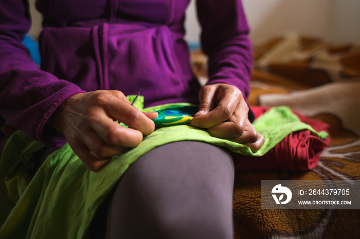 A woman sews a patch on torn clothes from an old sock.