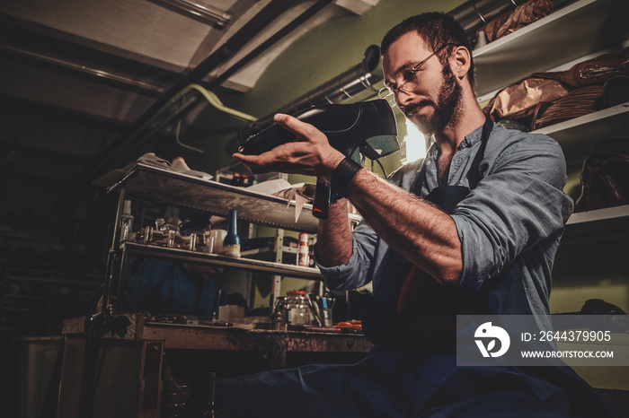 Talented cobbler is working on pair of black men’s shoes at his workshop.