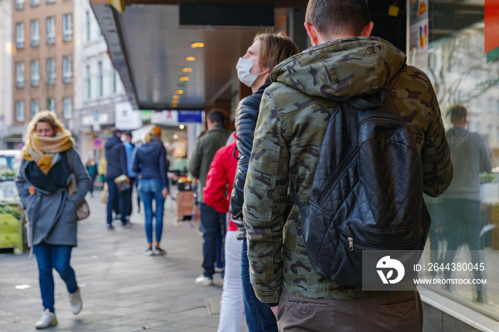 Selected focus, European people queue and wait on sidewalk outside in front of supermarket during quarantine for COVID-19 virus in Düsseldorf, Germany.