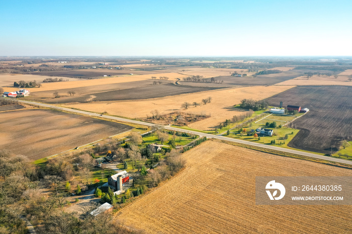 Beautiful aerial of farm land including barns, silos and a patchwork of agricultural fields in rural Wisconsin in autumn with patches of trees scattered throughout the landscape.