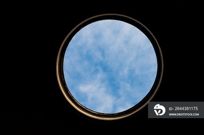 Large circular hole with golden frame and blue cloudy sky and black background.