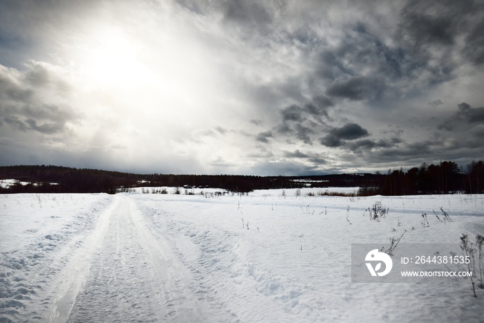 An empty country road with a sharp turn through the snow-covered field after a blizzard. Dramatic sky with glowing clouds. Karelia, Russia. Road trip, eco tourism, environmental conservation concepts