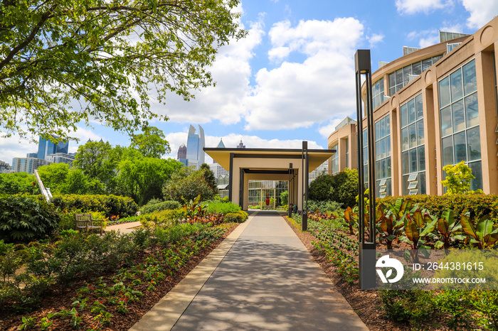 a long smooth footpath in the garden surrounded by lush green trees and plants with colorful flowers and buildings  with blue sky and clouds at Atlanta Botanical Garden in Atlanta Georgia USA