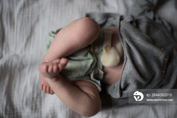 Neugeborenes Baby mit Nabelklemme und Wolle trägt grüne Stoffwindel und grauen Body und liegt auf Mulltuch oder Musselintuch