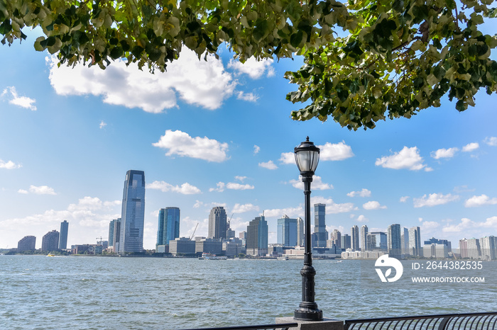 New Jersey skyline from Battery Park in a sunny day. Cityscape view through trees and streetlamp. City and travel concept. Manhattan, New York City, USA