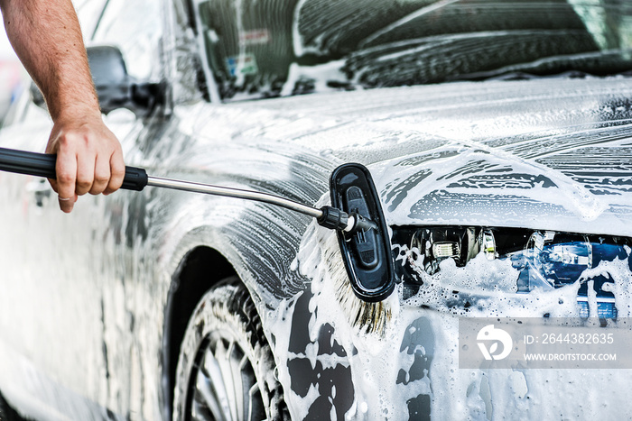 Man cleaning a car with brush and water.  Detal of washing a vehicle using a foam at touch less station.