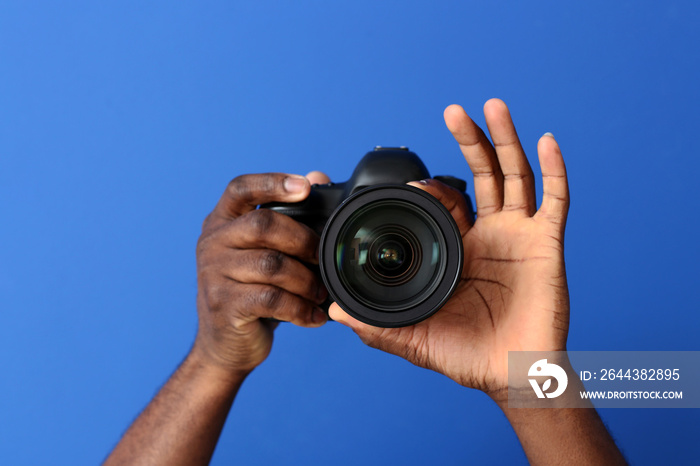 Hands of African-American photographer with camera on color background