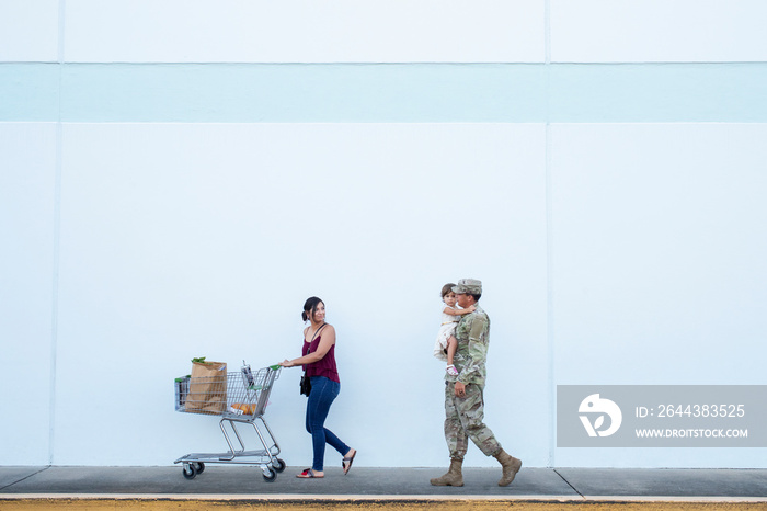 Woman pushes shopping cart while soldier holds his daughter