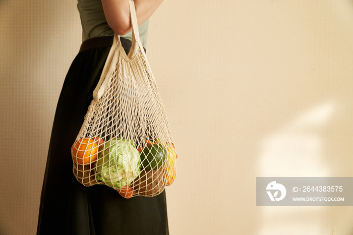 Woman hand holding a string shopping bag with vegetables, fruits in warm earthy tones, zero waste