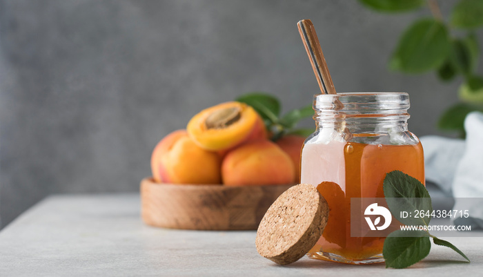 A jar with apricot jam and a spoon close-up on a gray. Fruit preservation. Copy space