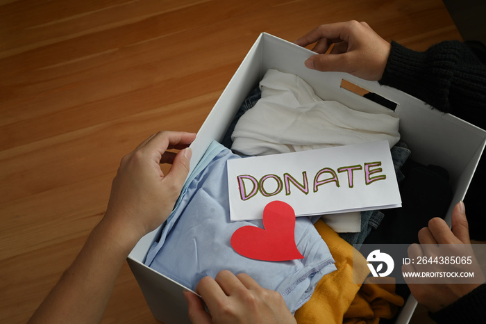 Top view of young volunteers holding box with clothes and donation lettering. Charity, donation and reuse recycle concept