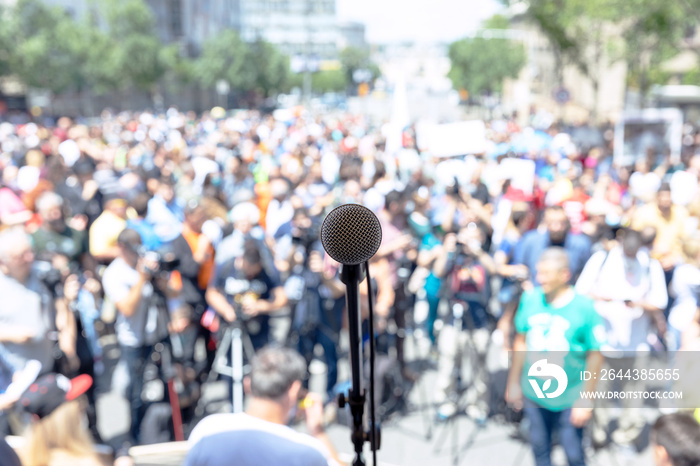 Focus on microphone, blurred group of people at mass protest or public demonstration in the background