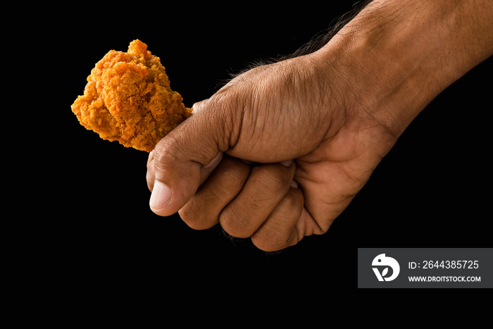 Close-up hand holding fried chicken on black background.