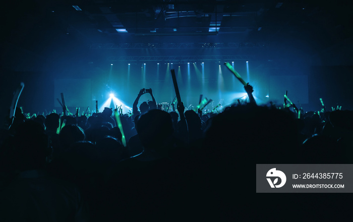 Silhouette audience crowd enjoy the club and raise hands with green light batons motion and use smart phone