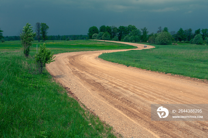 Yellow gravel road winding in a green field