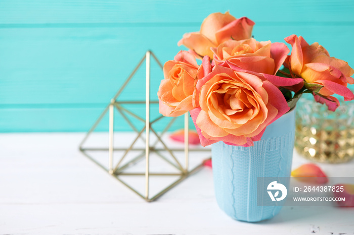 Bunch of fresh orange roses in blue cup on white wooden background against  turquoise  wall.