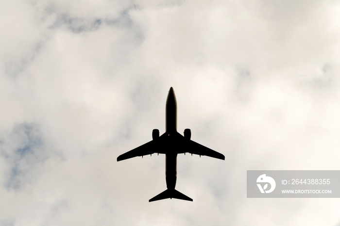 Silhouette of a large flying plane against a background of a cloudy sky, a bottom view