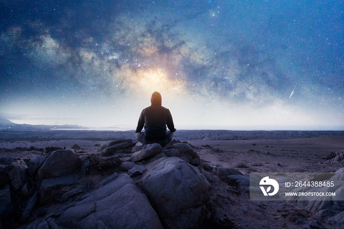 silhouette of a person sitting on the mountain meditating under de Milky Way and starry night, back view