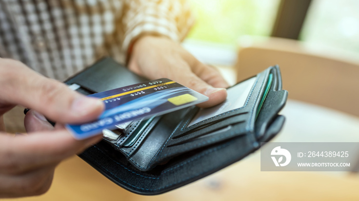 Young businessman giving credit card from wallet in coffee shop.