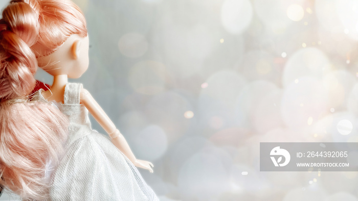 Magical photo. A doll in a white dress with pink hair stands with her back against a magical bokeh background