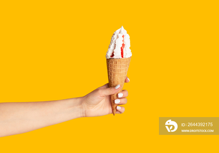 Young girl holding yummy ice cream with berry topping in waffle cone on orange background, close up of hand