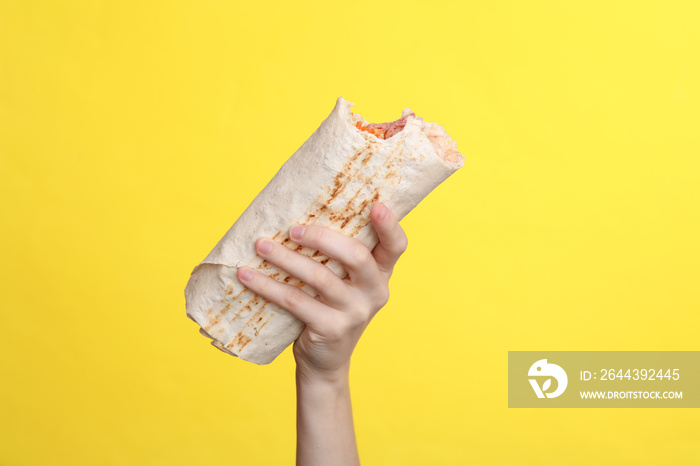 Woman’s hand holds appetizing bitten shawarma on a yellow background