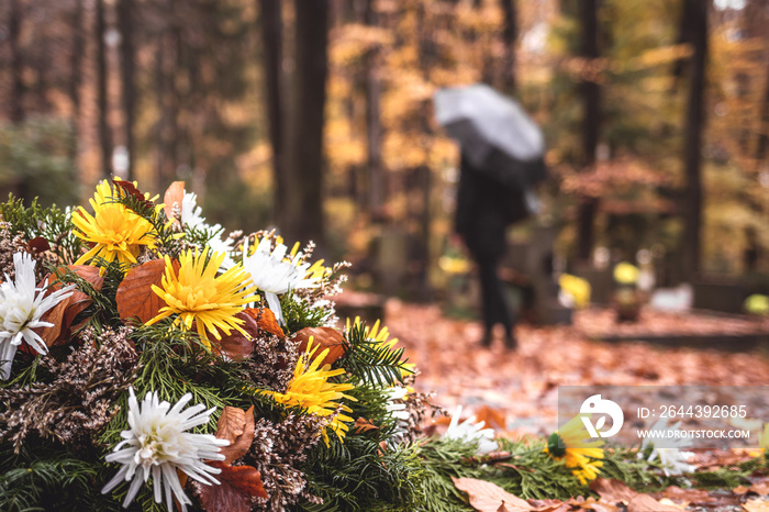 Flowers at tombstone. Defocused mourning woman holding flowers in hands and standing at grave in cemetery. Paying respect and last goodbye for dead person