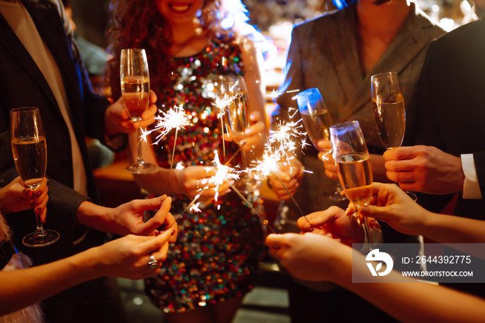 Sparkling sparklers in the hand. Group of happy people holding sparklers at the party. Young friends clinking glasses of champagne  in a nightclub. Celebration, people and holidays concept.