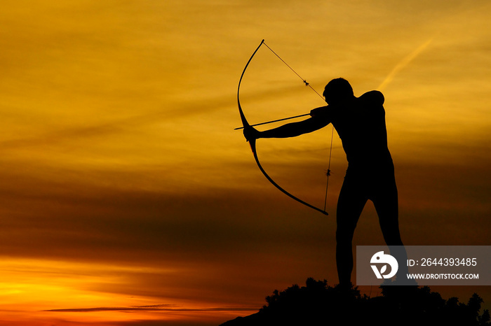 Silhouette of a handsome man with an ancient weapon bow and arrow on a background of sky and sunset.