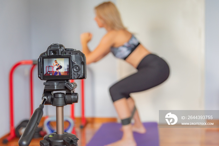 DSLR camera in front of fitness blogger recording a video blog about sports and home workout.