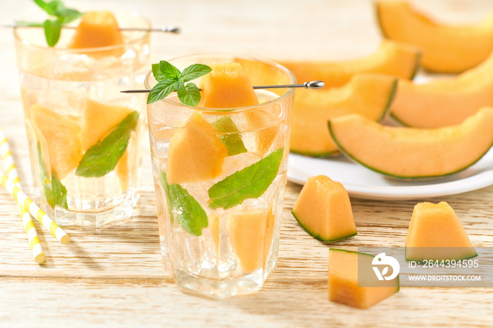 Melon lemonade with ice and mint in a glass on a wooden table. Melon drink in glasses with melon slices. melon water in glass jars.