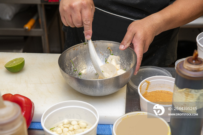 A Peruvian cook preparing ceviche with a citrus fish marinade in a stainless steel bowl