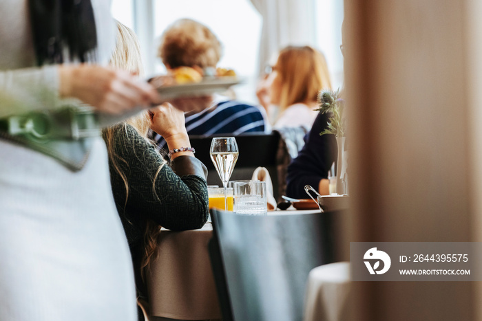 Glass of wine on table in restaurant with blurred officiant in foreground.