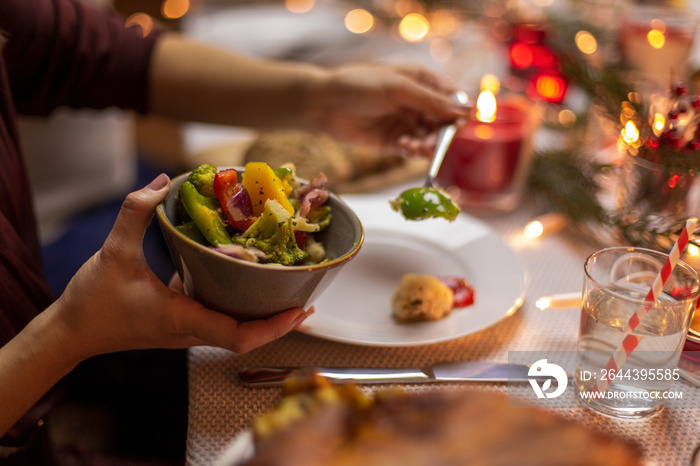 holidays, eating and food concept - close up of female hands with steamed vegetables in bowl at christmas dinner