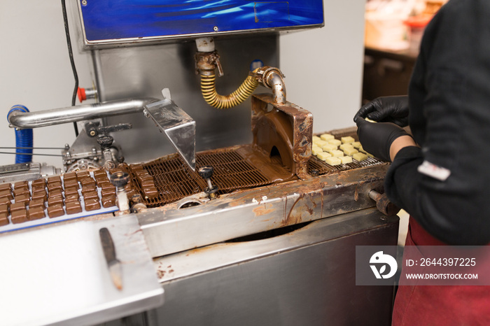 production, candy shop and people concept - confectioner making candies by chocolate coating machine at confectionery