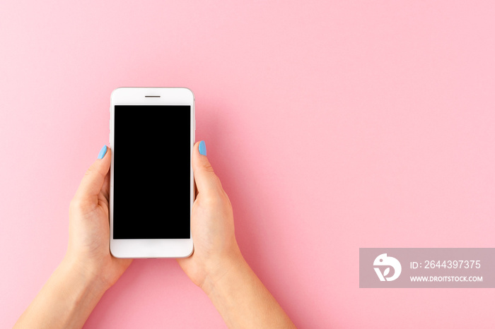 Female hands holding smart phone with empty screen on pink background. Top view