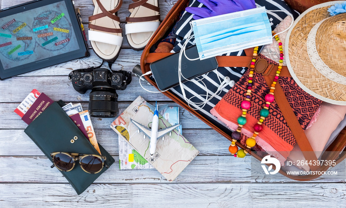 Above view of travel female accessories, luggage and personal items, camera, maps, boarding pass, facial mask due to coronavirus on wooden background - concept of travel safe