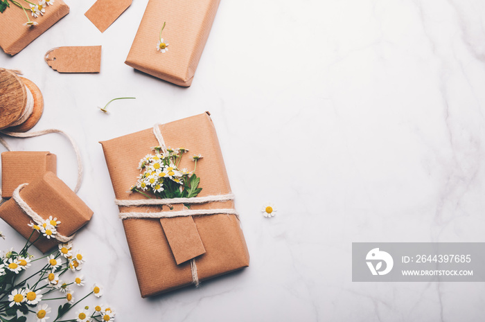 Gift wrapped in recycled brown paper decorated with real fresh chamomiles, on light background with minimalist style wrapping, top view flat lay, eco friendly and zero waste packaging