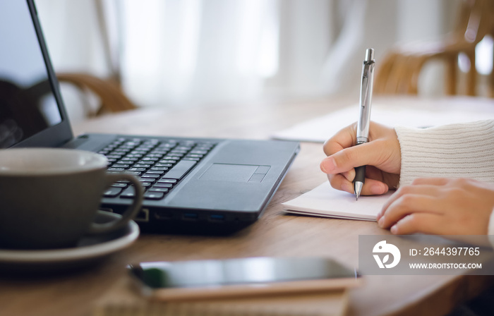 Close-up. girl hand writing on paperwork while she working with laptop on desk