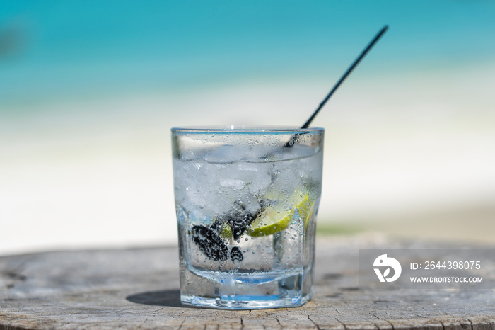 Soda water with lime and ice on a wooden table near the sea on the beach